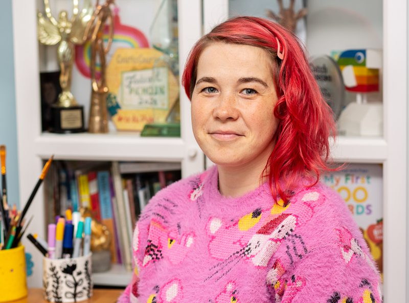 Evgenia Golubeva in a pink jumper, in front of a shelf of awards and books